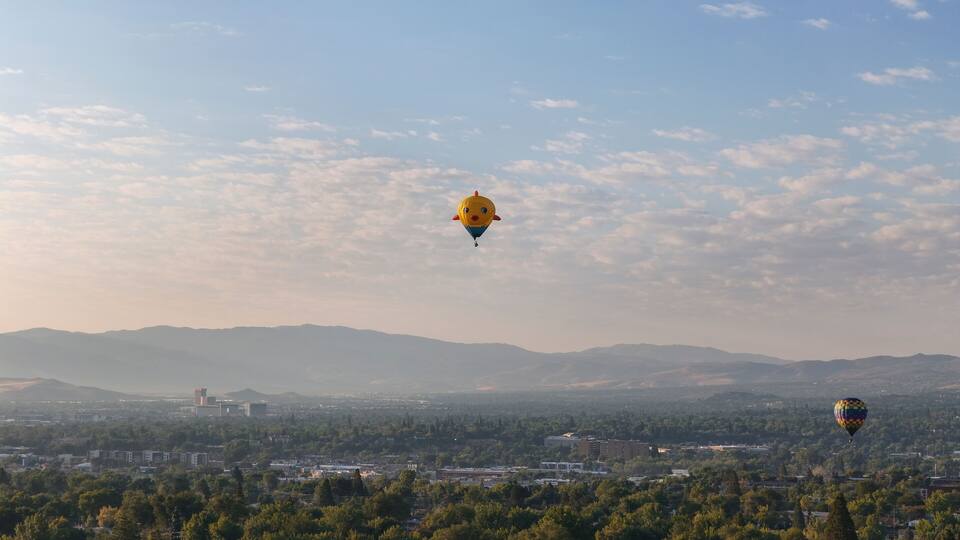 Aerial view of colorful hot air balloons over a scenic landscape with mountains and cityscape, Old Northwest, Reno, Nevada, United States.