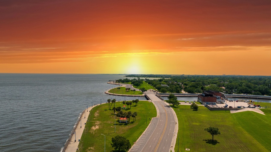 Aerial shot along the coast of Lake Pontchartrain with lush green trees and grass at Lakeshore Park in New Orleans Louisiana USA