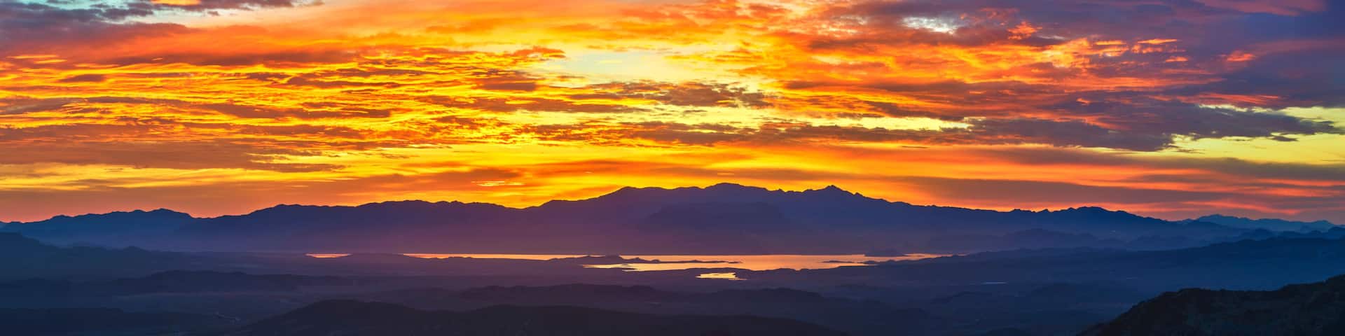 A mountain range with a lake at its base, under a vibrant sunset sky.