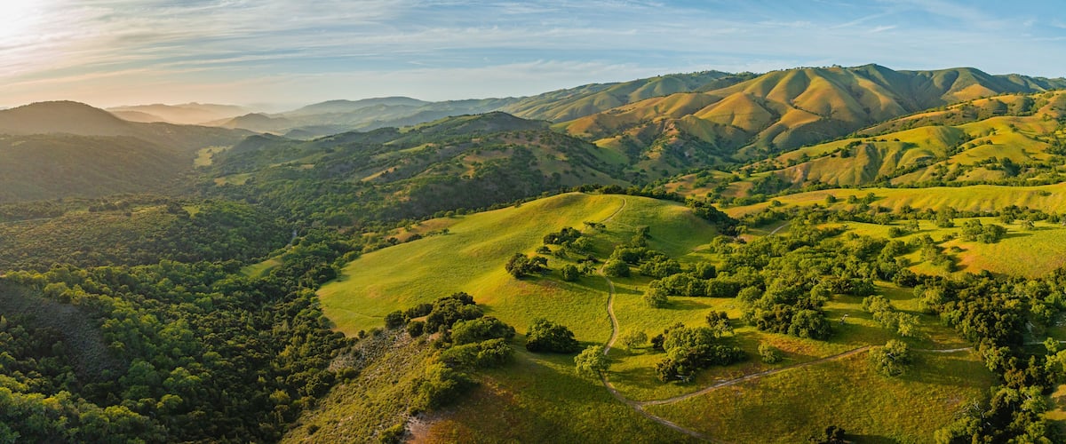 Panoramic drone aerial view of length of Carmel Valley at sunset. Green rolling hills with golden glow.