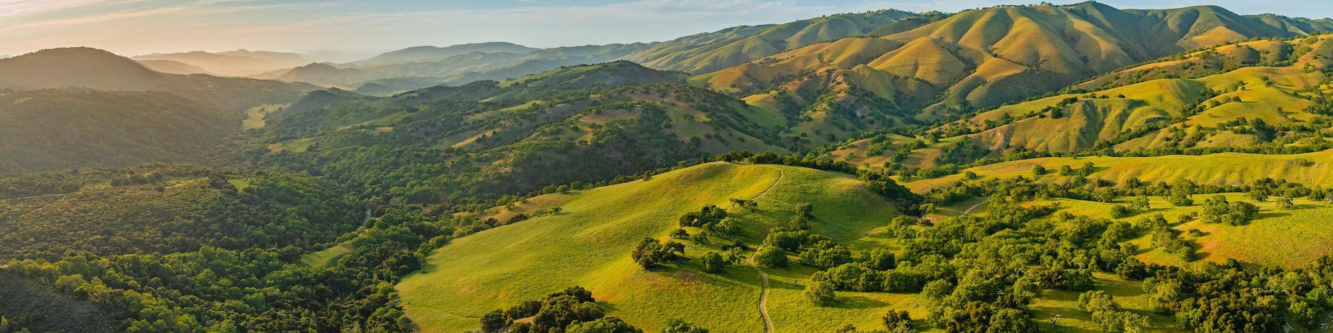 Panoramic drone aerial view of length of Carmel Valley at sunset. Green rolling hills with golden glow.