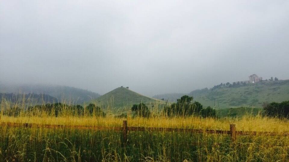 A grassy field with a wooden fence, rolling hills, and a distant building.