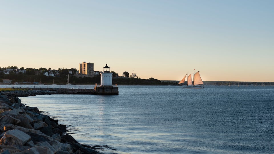 Bug light lighthouse in Portland, Maine at sunset as a sailboat sails into the harbor