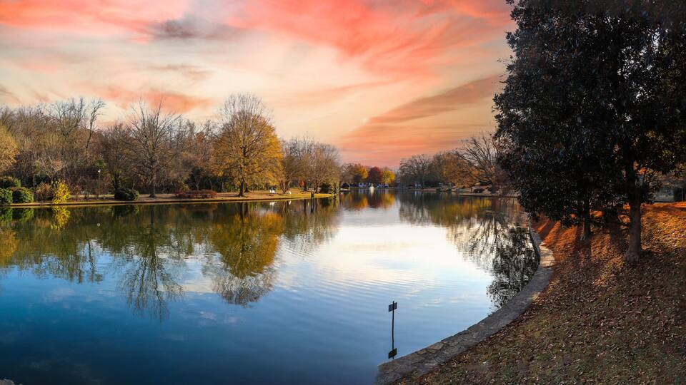 a panoramic shot of a gorgeous autumn landscape with lake and autumn colored trees reflecting off the water with red sky and clouds at sunset at Freedom Park in Charlotte North Carolina USA