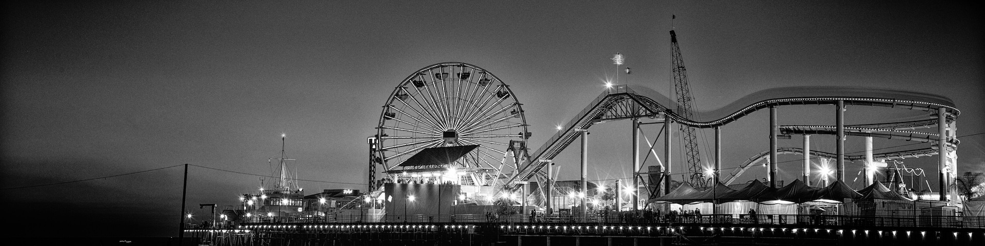 Parque de diversões à noite, com roda gigante, montanha-russa e uma atração circular grande.