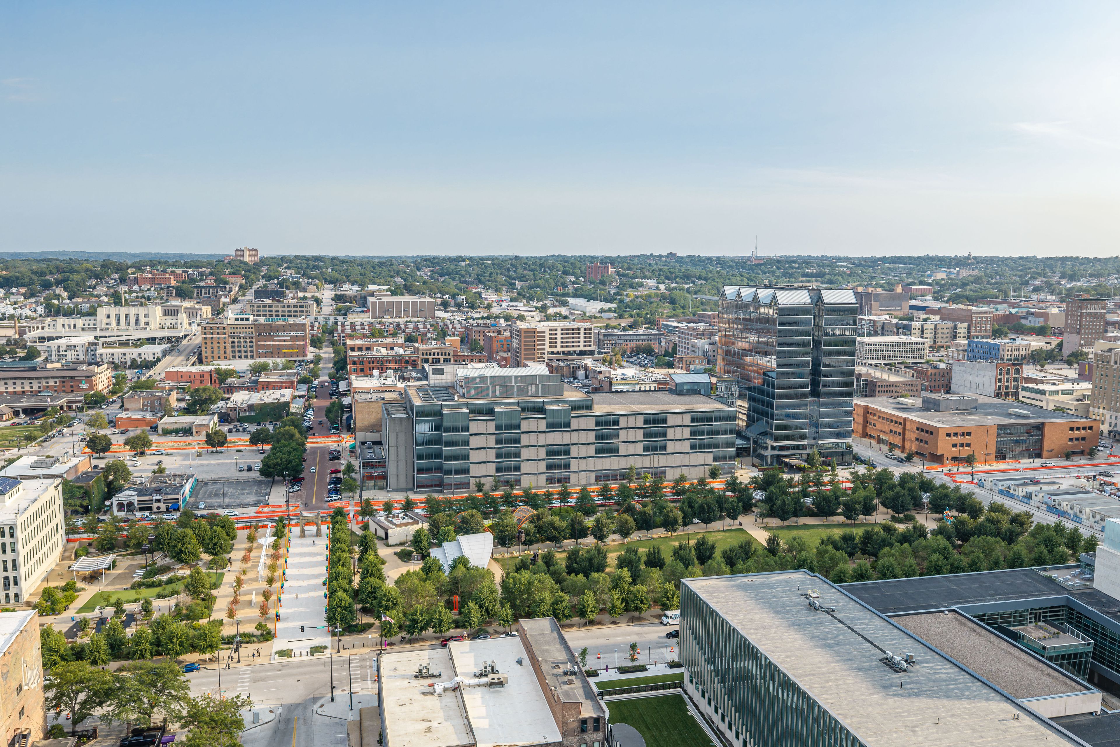 A cityscape with modern buildings, a clear sky, and a distant view of a hilly landscape.