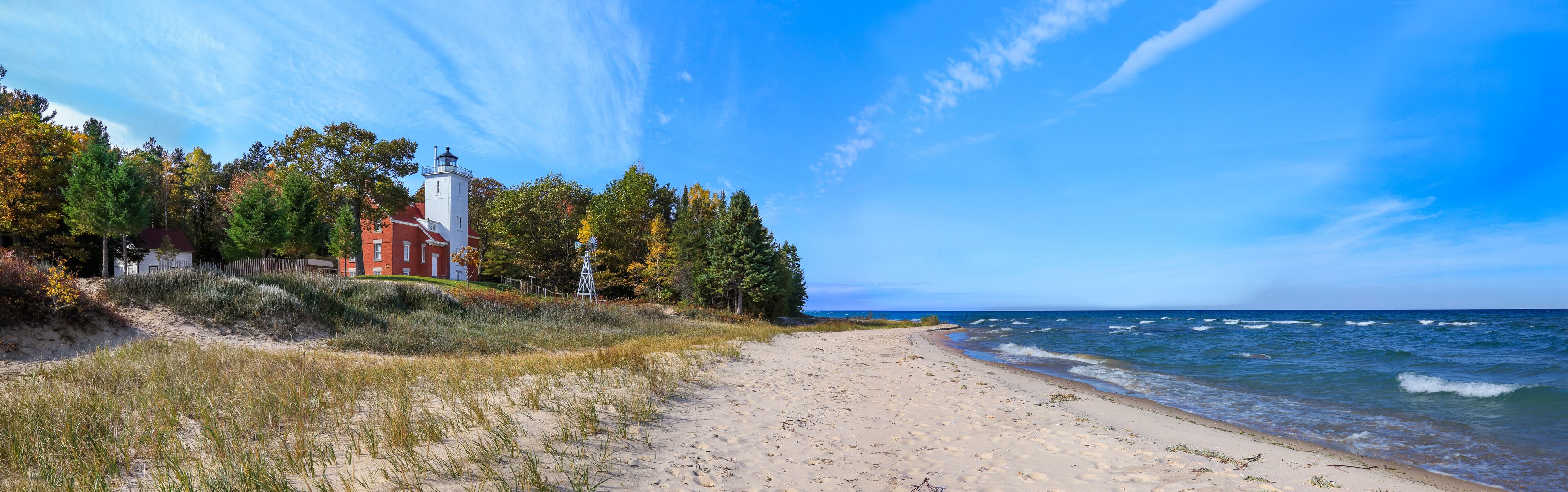 A beach with a lighthouse and a red building on the shore.