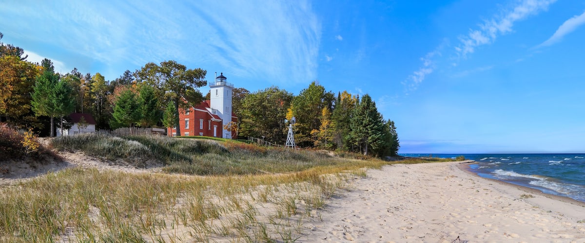 A beach with a lighthouse and a red building on the shore.