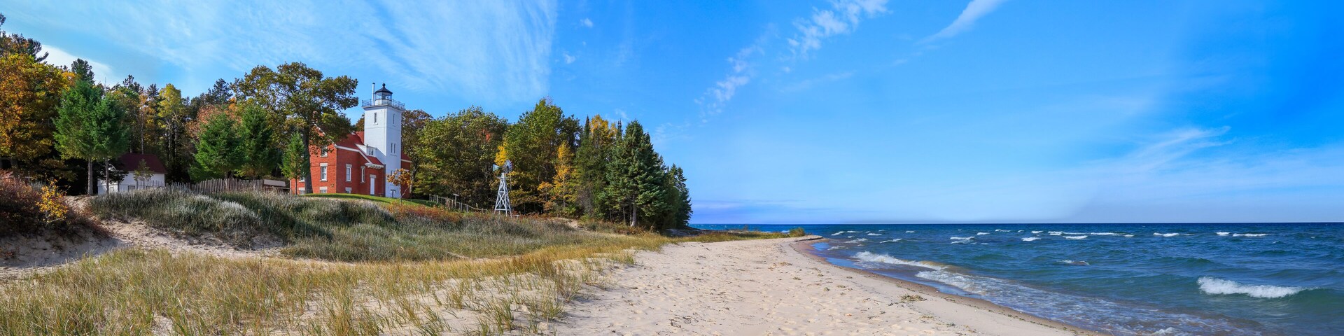 A beach with a lighthouse and a red building on the shore.