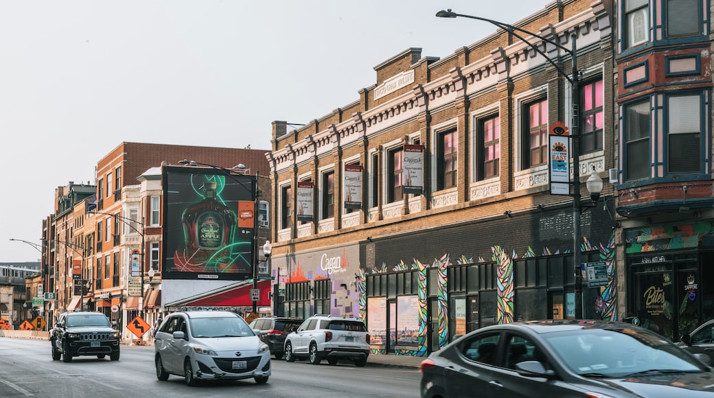 A street lined with multi-story buildings, some with commercial establishments and signage, and cars parked along the street.