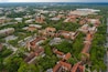 An aerial view of a historic town with red-roofed buildings, a large stadium, and surrounding greenery.