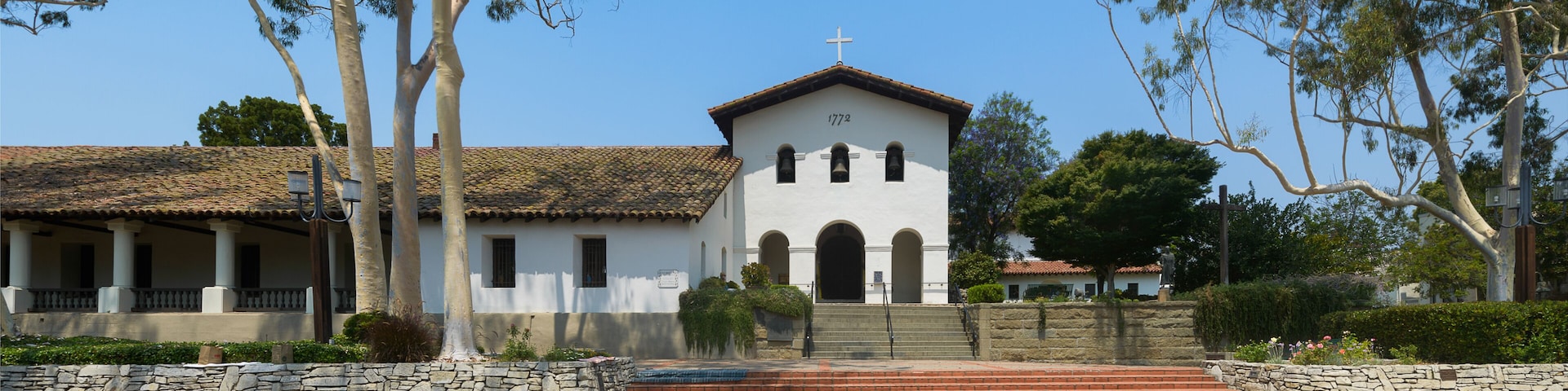 Une Ă©glise blanche surmontĂ©e dâune croix, entourĂ©e dâarbres et dâun mur de pierre.