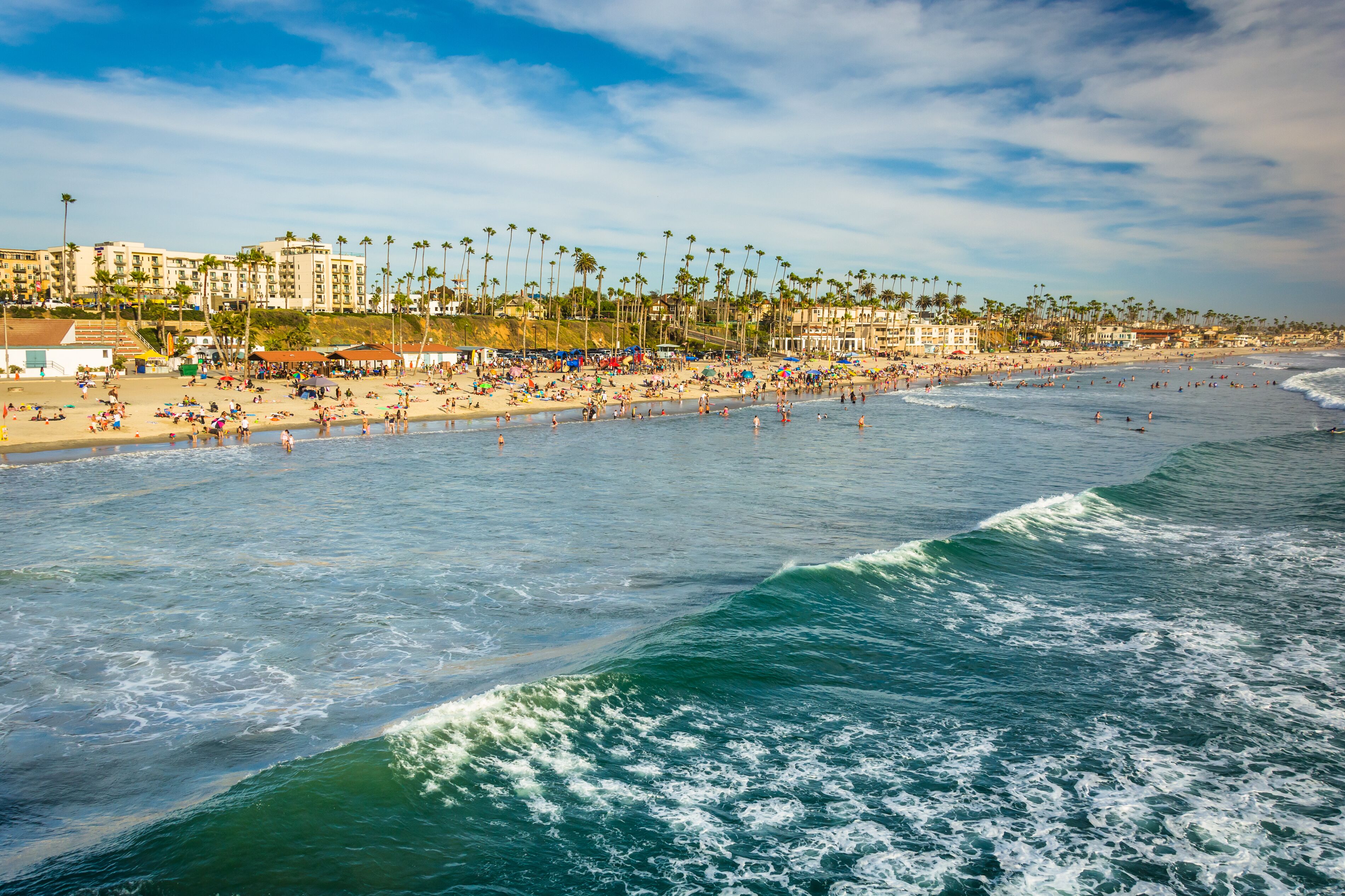 A beach with palm trees, people, and buildings in the background.