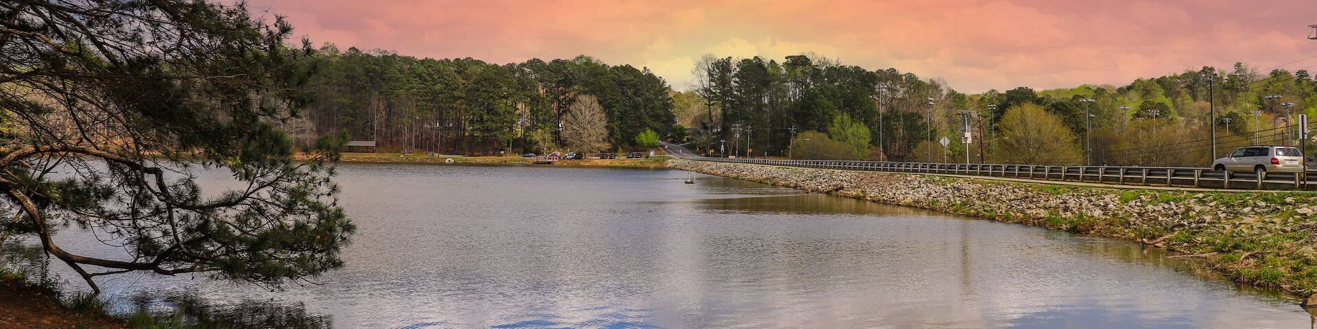 a stunning shot of the vast still waters of a lake surrounded by lush green trees with powerful clouds at sunset at Murphey Candler Park in Atlanta Georgia USA