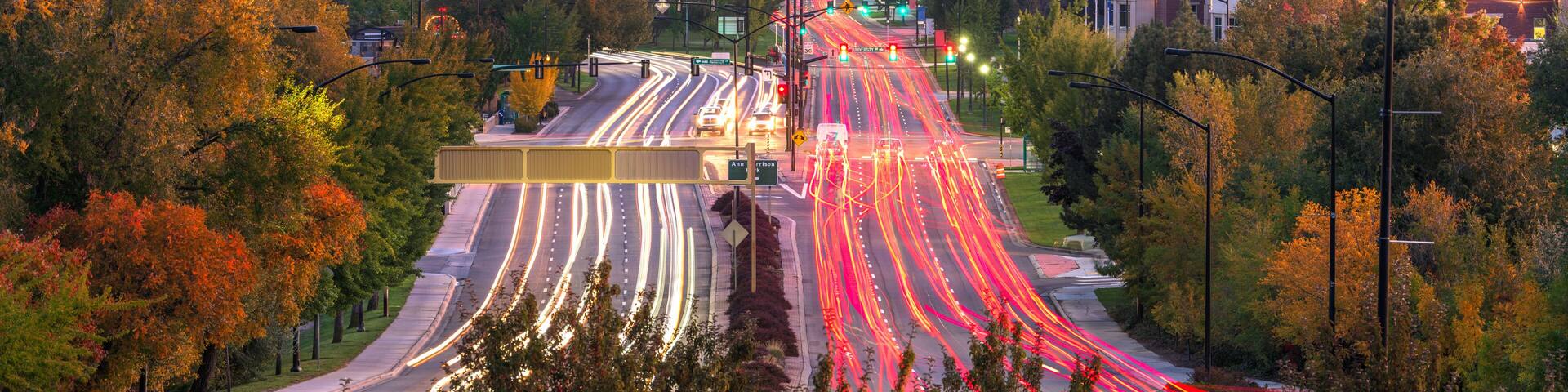 A cityscape with a multi-lane highway, autumn trees, and a mountainous backdrop.