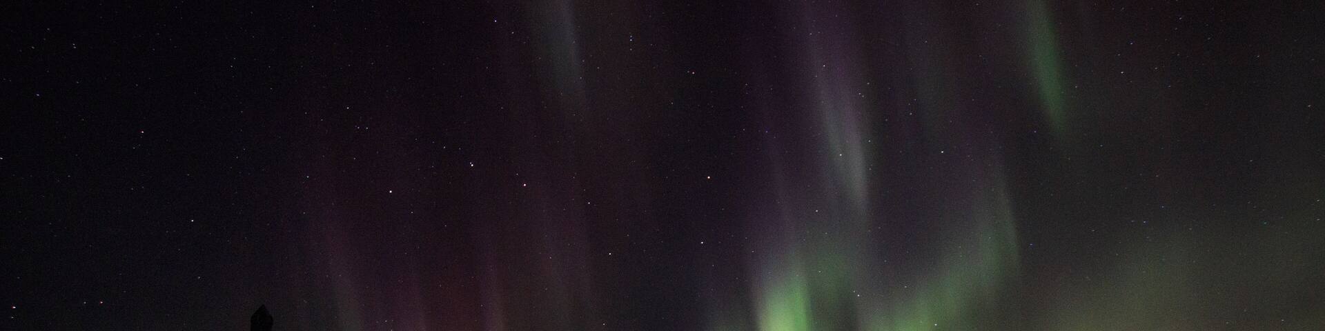 The Northern Lights over a calm lake with mountains in the background.