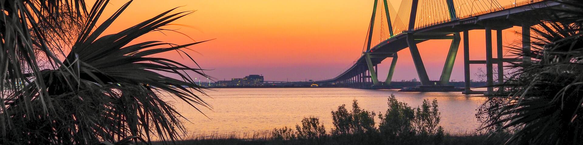 A bridge at sunset with a clear sky and water in the foreground.