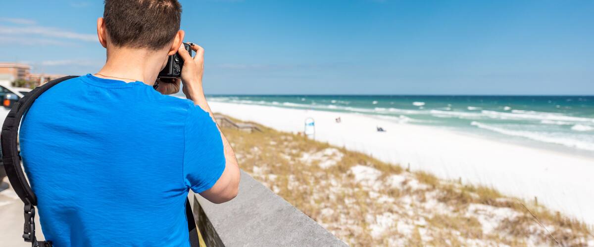 Destin Miramar beach city town village in Florida panhandle gulf of mexico ocean with photographer young man closeup in blue shirt taking picture photo of sand dunes with camera