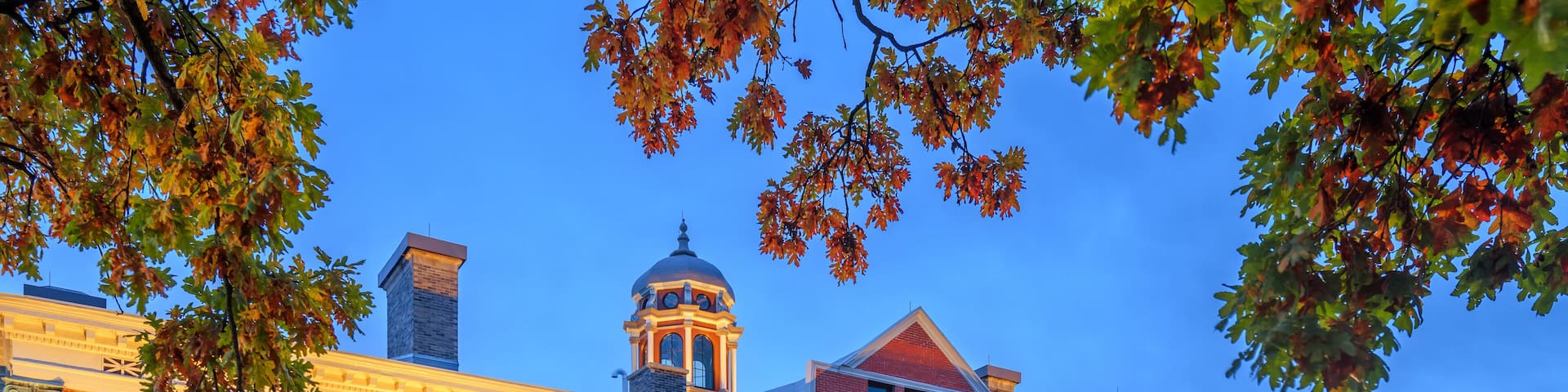 A large brick building with a dome and a clock tower, surrounded by a well-maintained lawn and autumn foliage.