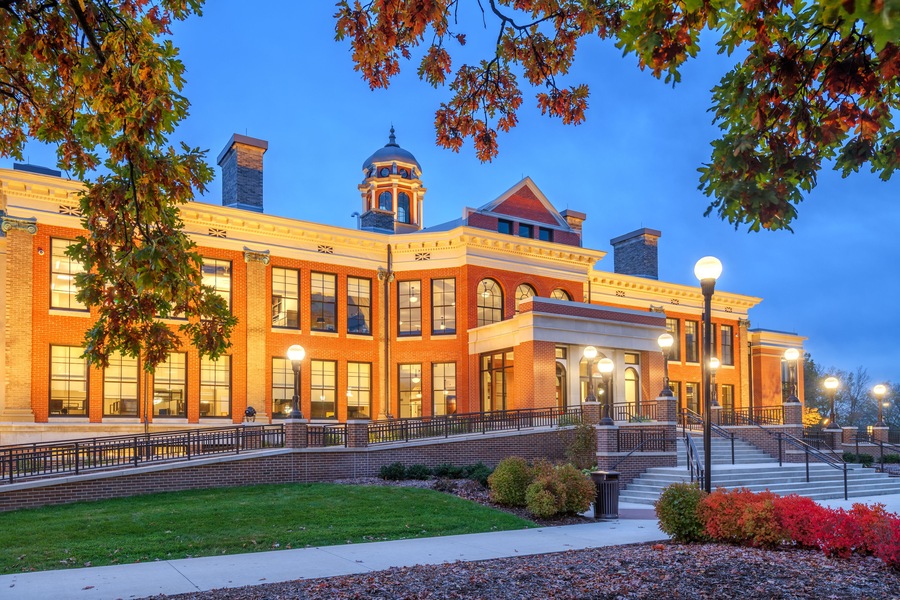 A large brick building with a dome and a clock tower, surrounded by a well-maintained lawn and autumn foliage.