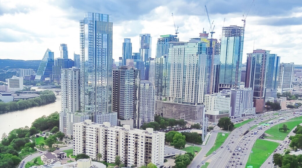 Panorama aerial view Austin Downtown skyscrapers along lush green curved Colorado River, high rise office buildings under construction, fast growing Texas Capital City, modern skyline hotel condo