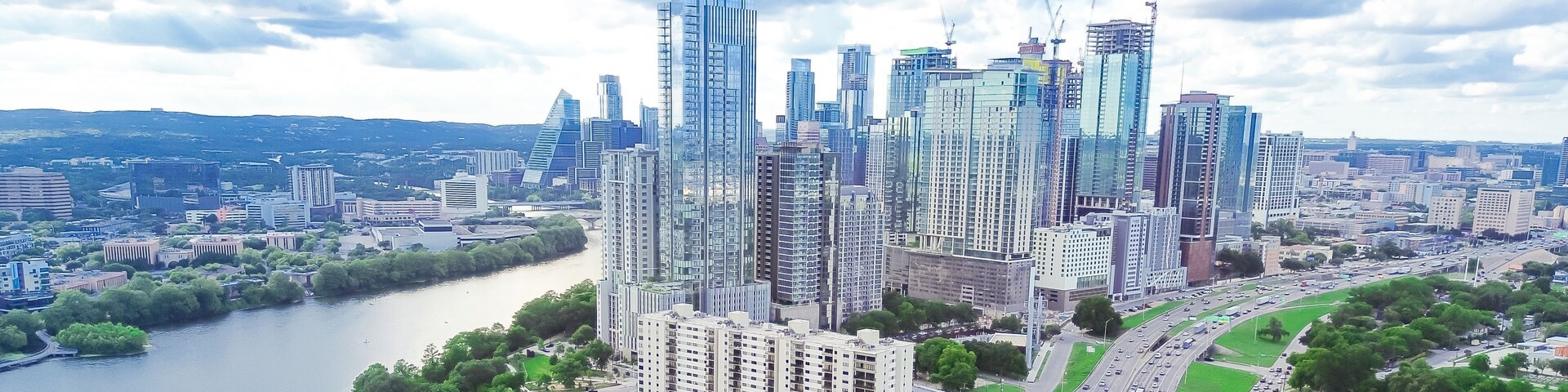 Panorama aerial view Austin Downtown skyscrapers along lush green curved Colorado River, high rise office buildings under construction, fast growing Texas Capital City, modern skyline hotel condo