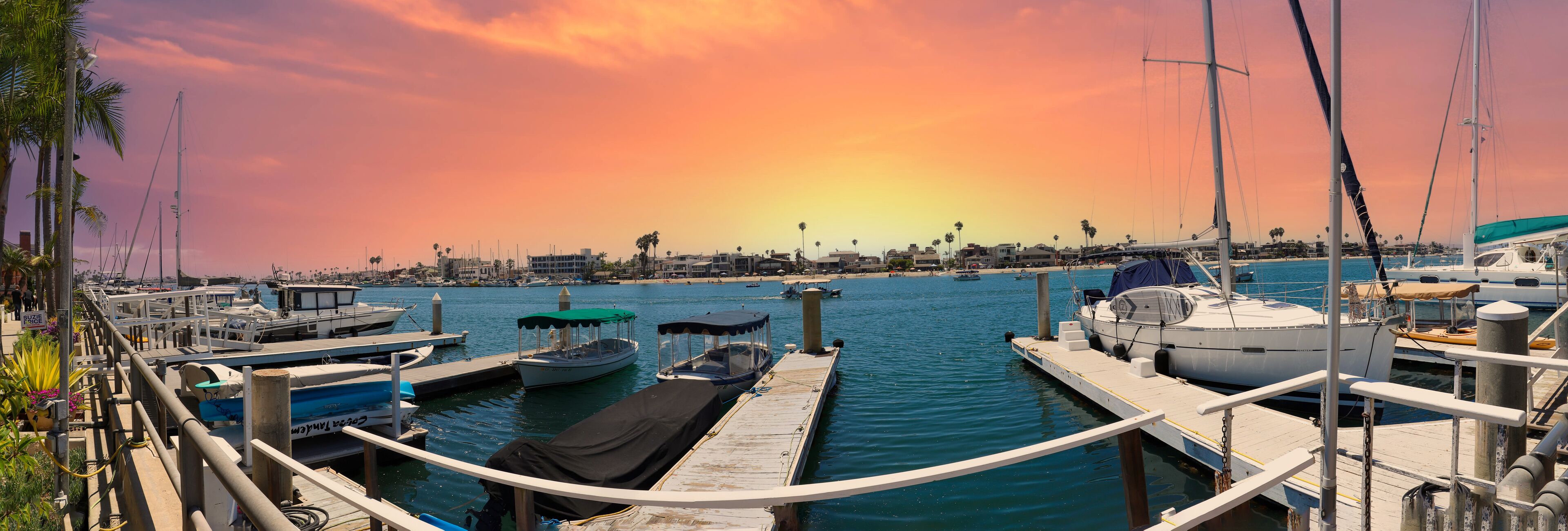 a gorgeous summer landscape at Naples Canals with people on paddle boards on blue ocean water with boats docked along the banks and homes with lush green palm trees and powerful clouds at sunset