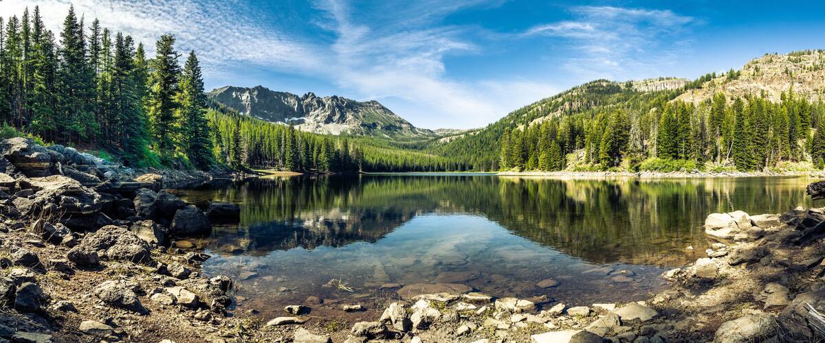 Panorama of a mountain lake with rocks in the foreground and trees in the far shore with mountains in the background, blue sky with high clouds. Strawberry Lake, Strawberry Wilderness, Oregon