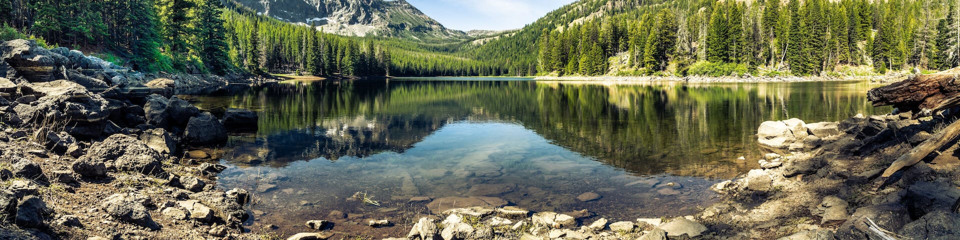 Panorama of a mountain lake with rocks in the foreground and trees in the far shore with mountains in the background, blue sky with high clouds. Strawberry Lake, Strawberry Wilderness, Oregon