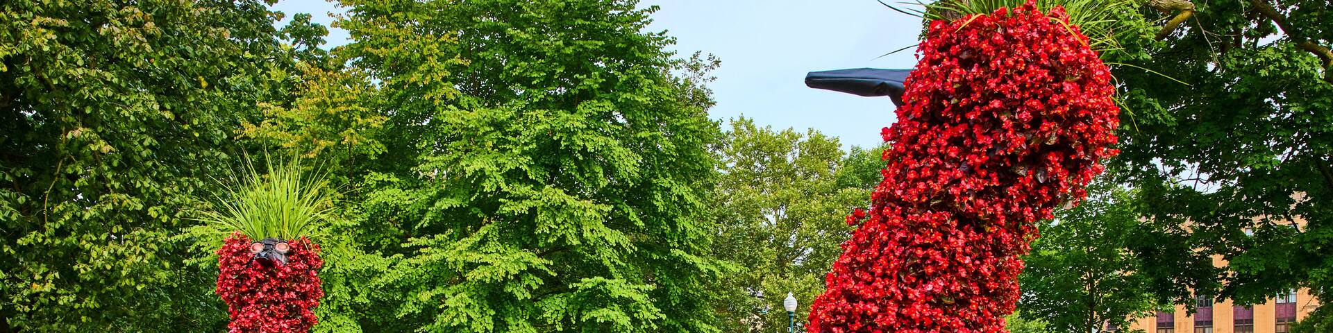A park with large floral sculptures of animals and a building in the background.