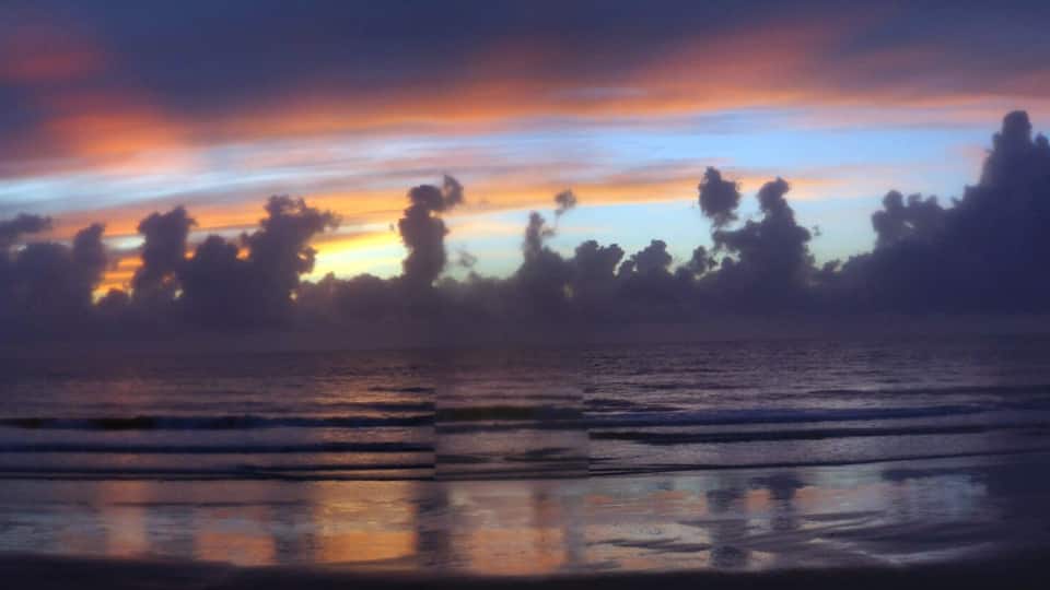 A beach at sunset with waves reflecting the sky.
