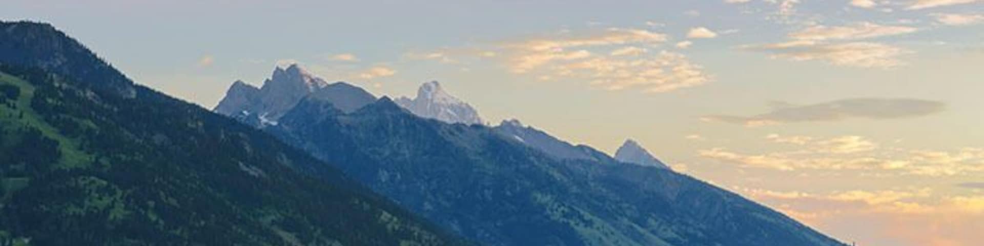 Just before dawn and the early sunlight is illuminating the skies and the Grand Tetons. 
It was mid-July when this photo yet the mountains have snow on them still.