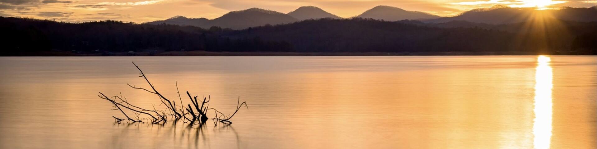 A calm lake at sunset with mountains in the background.
