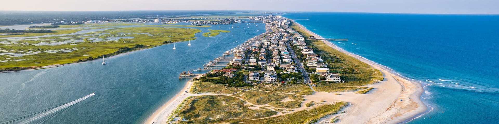 An aerial view of a coastal town with a long beachfront, clear blue waters, and a marina.