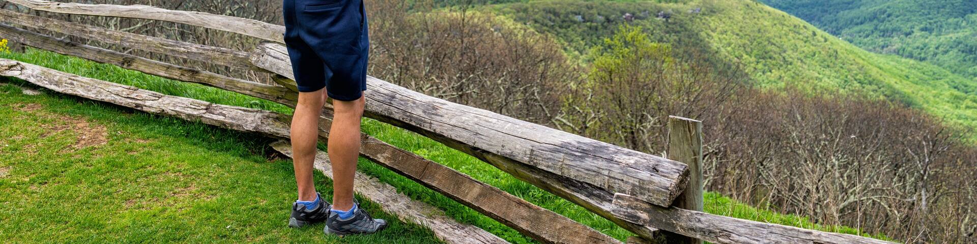 A person taking a photo of a mountainous landscape with a wooden fence in the foreground.