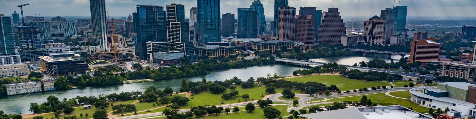 A city skyline with modern skyscrapers, a river, and a park with winding paths.