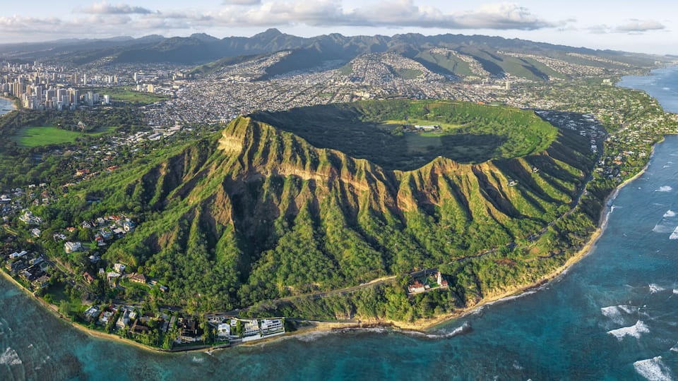 An aerial view of a lush, mountainous island surrounded by clear blue waters.