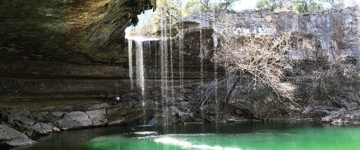 A cave with a waterfall and a green pool.