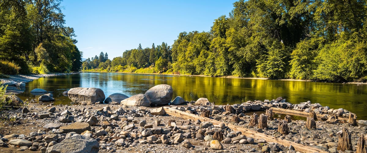 Autumn Rogue River and Riverside park forest landscape over the rocky beach with ruined pilings in Grants Pass, Oregon