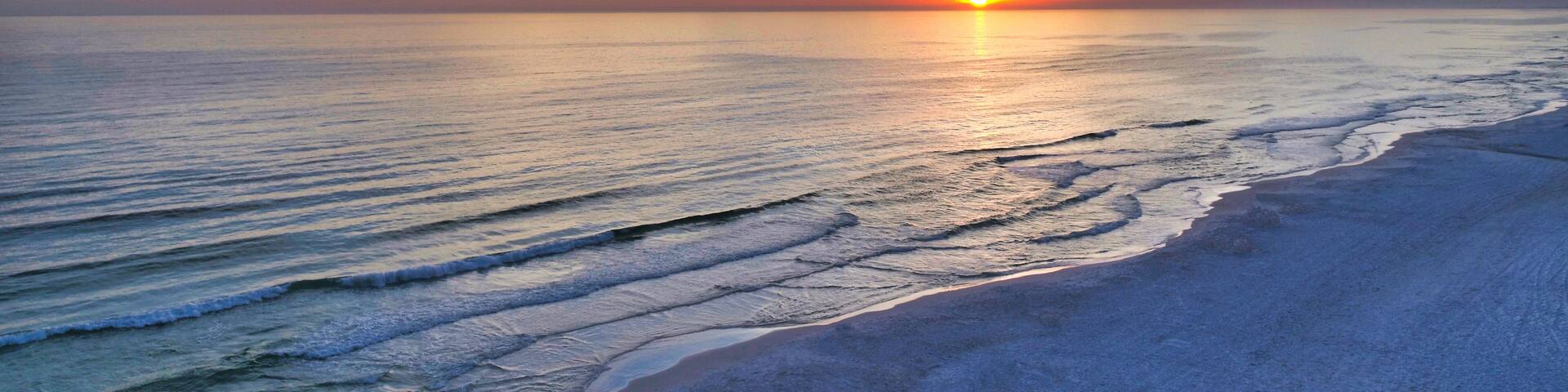 A sunset over a beach with waves and a clear sky.