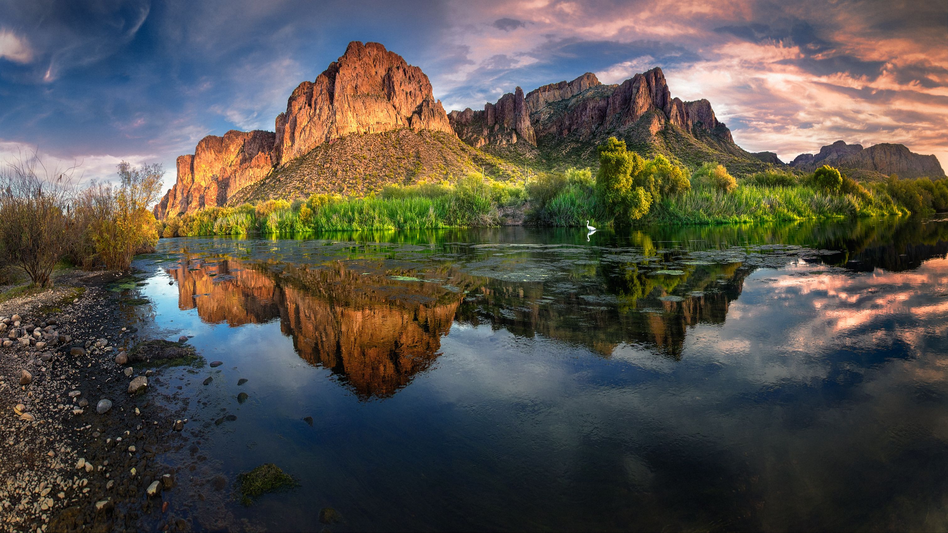 Un río tranquilo que refleja un paisaje montañoso con un pico destacado y abundante vegetación.