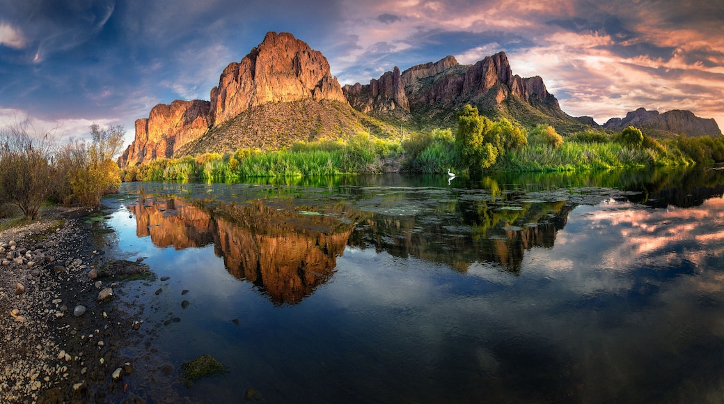 Un río tranquilo que refleja un paisaje montañoso con un pico destacado y abundante vegetación.