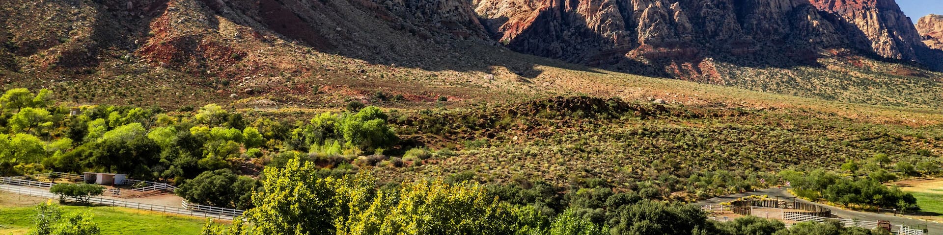 Beautiful view of famous Spring Mountain Ranch State Park near Las Vegas and Red Rock Canyon, Nevada during autumn with pink and red rock mountains, blue sky, green trees and grass, and purple hills