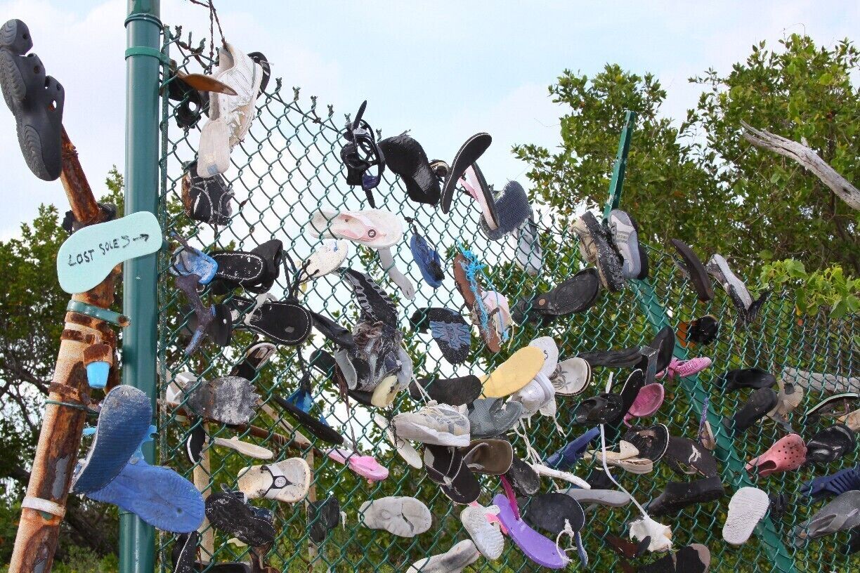 A fence with numerous lost shoes hanging on it.