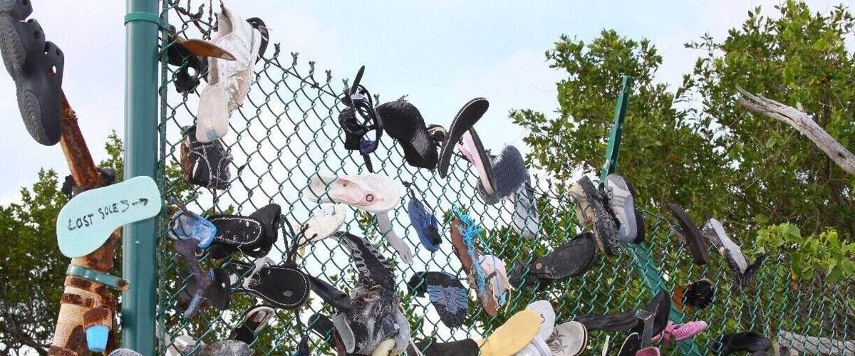 A fence with numerous lost shoes hanging on it.