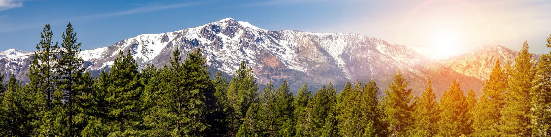 Panoramic landscape scene with sun shining behind the snow capped mountains in Lake Tahoe California