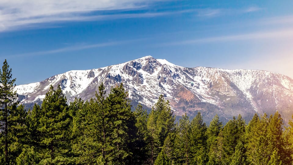 Panoramic landscape scene with sun shining behind the snow capped mountains in Lake Tahoe California