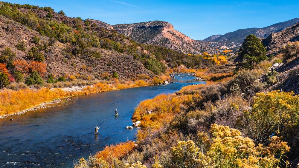 Ein Fluss fließt durch eine gebirgige Landschaft mit herbstlich gefärbten Bäumen.
