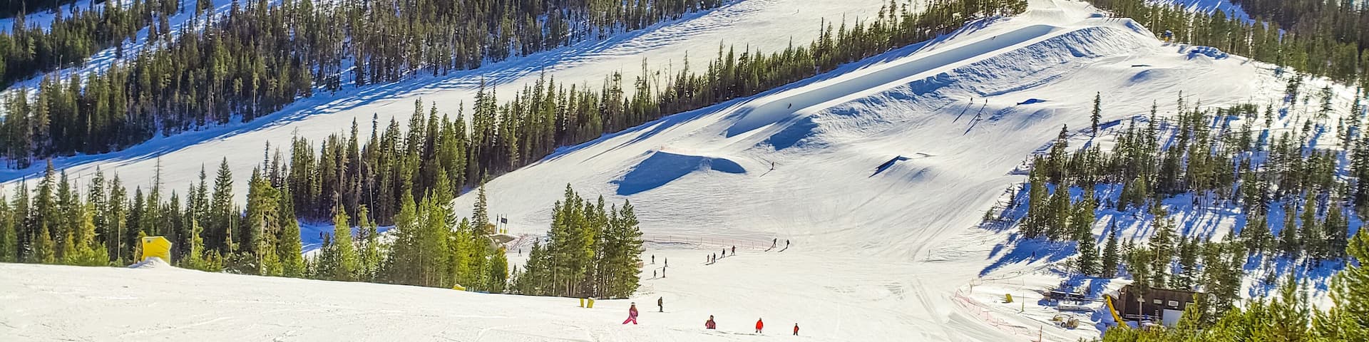 View of ski slope with terrain park and woods in Colorado ski resort on nice winter day; blue sky in background