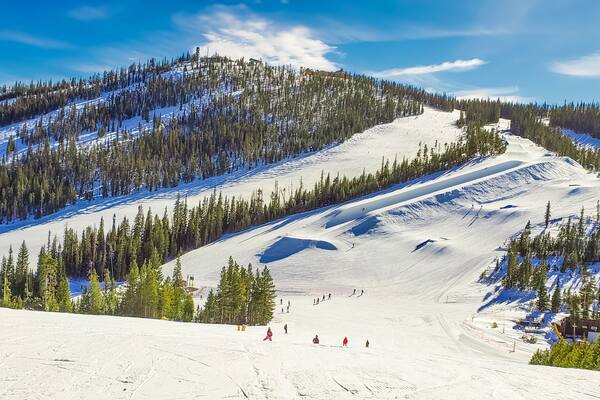 View of ski slope with terrain park and woods in Colorado ski resort on nice winter day; blue sky in background